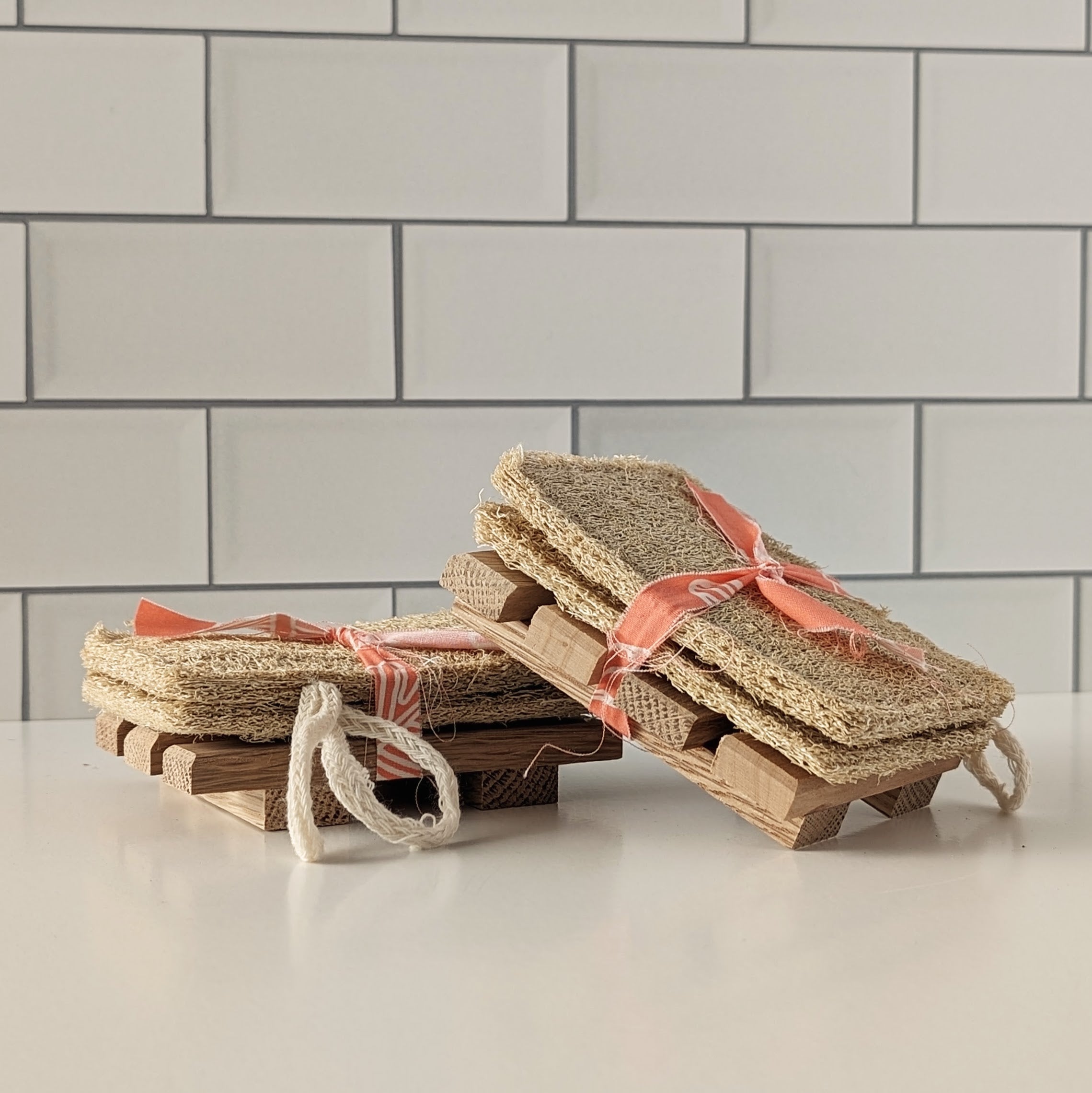 Set of natural fiber scrubs on wooden stands against a tiled wall background