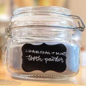 Closeup photo of a glass jar filled with black powder labeled "charcoal + mint tooth powder"