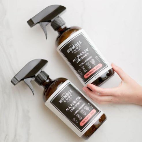 Two brown bottles of all purpose cleaner. Spray to remove bottle top, squeeze trigger to spray, twist tip to close. White cloth background.