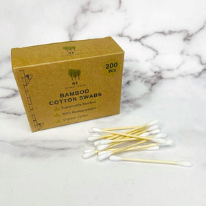 Handful of bamboo stick cotton swabs next to box of cotton swabs.