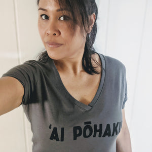 Hawaiian woman wearing a soft lightweight dark gray v-neck women's tee with 'AI PŌHAKU in black ink on the chest