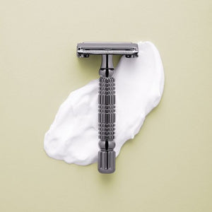 Rockwell R1 Double-Edge Safety Razor in Gunmetal (Gray Color) shown on a smear of white shaving cream on a neutral green background 